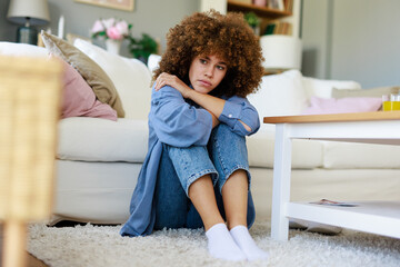 Curly-Haired Woman Feeling Unwell in a Bright Living Room with Cozy Furniture and Natural Light