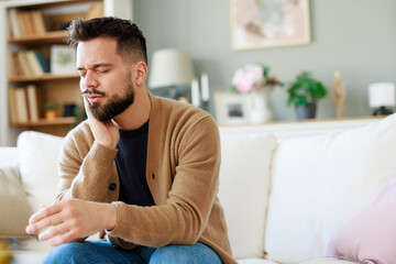 Young Man in Beige Cardigan Expressing Discomfort in Well-Lit Living Room with Neutral Decor