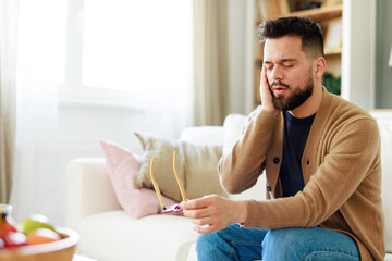 Bearded Man In Casual Attire Experiencing Neck Discomfort While Checking Phone In Sunlit Living...