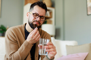 Caucasian Male in His 30s Holding Medicine and Water Glass in a Comfortable Living Room