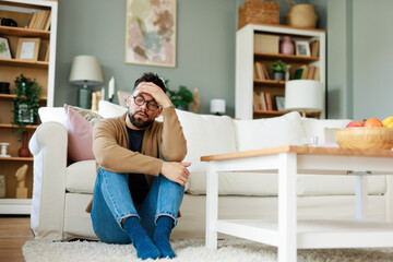 Young Caucasian Man Sitting on Living Room Floor Looking Stressed in a Comfortable Home Setting