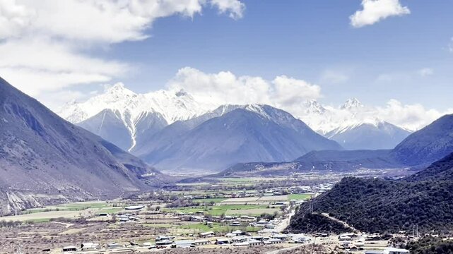 Blue sky, white clouds, snow - capped mountains and farmland in the valley