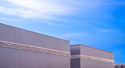 Row of factory warehouse industrial buildings with ventilation louver on gray aluminium corrugated metal wall against blue sky background, Perspective side view with copy space