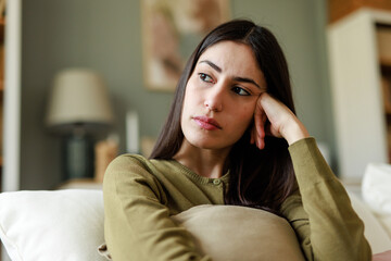 Young Woman in Green Sweater Sitting on Couch with a Thoughtful and Pensive Expression