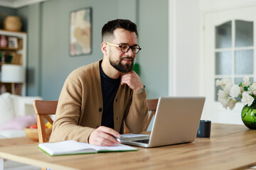 Young Caucasian Man Working Remotely in a Cozy Home Office Setting with Laptop and Notebook