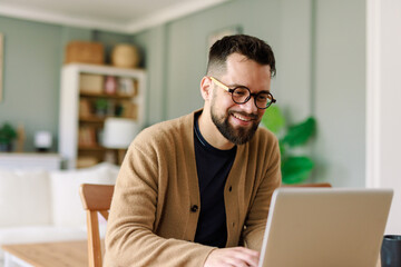 Smiling Young Caucasian Man in Glasses Working Remotely from Home in a Warm and Cozy Living Room
