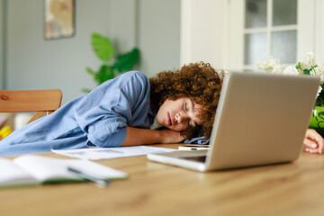 Young Woman Resting on Desk in Home Office with Laptop and Documents on a Wooden Table