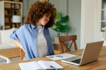 Woman In Blue Button-Down Shirt Stretching Due To Back Discomfort During Remote Work At Home Office