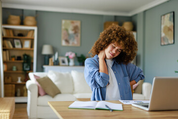 Young Woman with Curly Hair Feeling Neck Pain While Working from Home in a Cozy Indoor Setting
