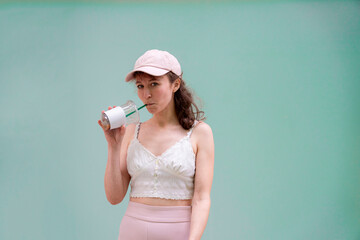 A stylish young woman enjoying a drink in a light summer outfit against a pastel background evoking summer