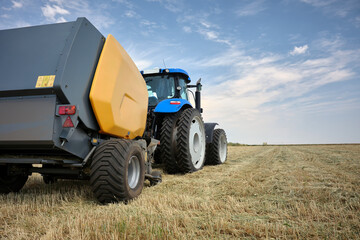 Tractor with equipment for collecting dry hay. Mown ears of wheat lie on the ground in a field.