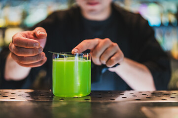 Bartender preparing vibrant green cocktail with garnish, showcasing mixology skills and attention to detail in a modern bar setting