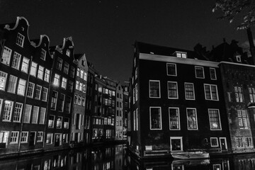 Black-and-white rendering of the same Amsterdam canal view. Bright window lights stand out against...