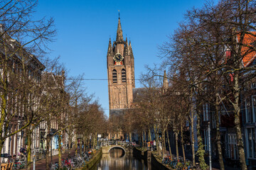 Bright winter morning in Delft. The brick tower of the Nieuwe Kerk stands at the canal’s end, its...