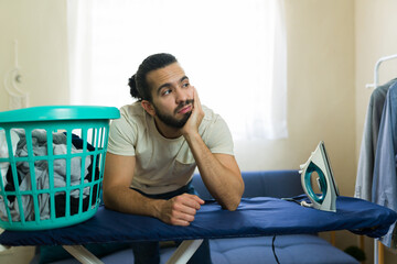 Frustrated man leaning on ironing board contemplating house chores