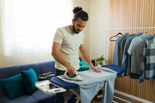 Young man ironing clothes at home doing housework