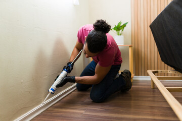 Handyman caulking baseboard in bedroom during home renovation