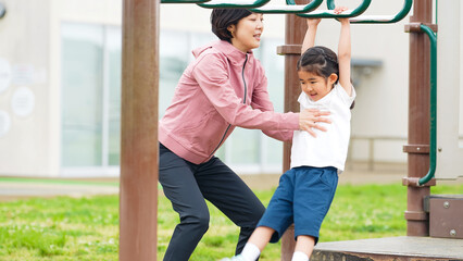 公園の雲梯で遊ぶ女の子と補助する女性