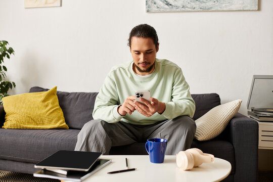 Young handsome man relaxing at home while using his smartphone and enjoying a cup of coffee