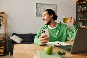 Young man enjoying a relaxed moment at home while sipping tea and using his smartphone