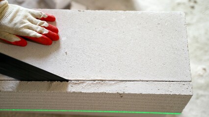 Construction worker cutting aerated concrete block with hand saw and laser level