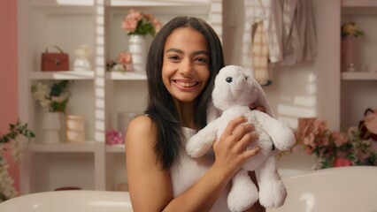 Smiling Hispanic girl ethnic happy beautiful Latina teen female hugging soft fluffy rabbit toy...