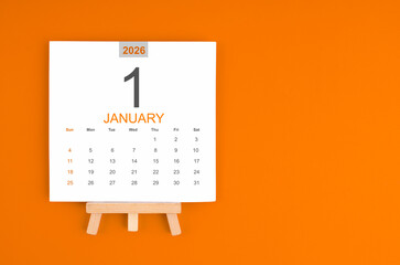 Calendar page for January 2026 with wood easel on orange color background.