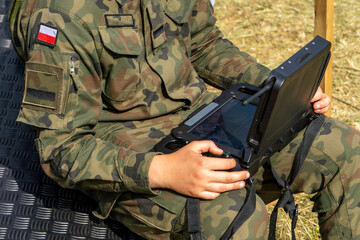 Soldier in camouflage uniform operating a military rugged tablet outdoors – modern technology in...