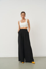 Stylish woman poses in fashionable crop top and wide-leg pants in a studio setting