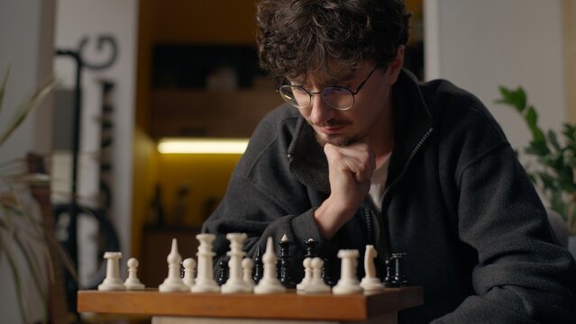 Contemplative Caucasian guy player grandmaster playing chess board game at home pensive smart male moving pawn piece chessboard thinking man pondering strategy gaming tactics preparing for tournament - Powered by Adobe