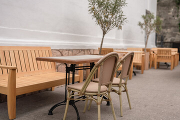 Cafe Table Chairs: Outdoor cafe with wooden furniture, trees, set up daytime for relaxing.
