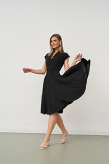 Beautiful female model in stylish black dress posing indoors in a studio setting