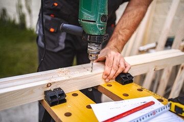 Unrecognizable male carpenter using electric drill on a wooden plank outdoors