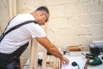 Mature male carpenter using electric screwdriver on a wooden plank outdoors
