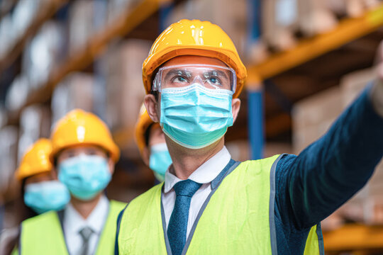 Workers in safety gear and face masks inspect and manage inventory in a warehouse or industrial setting. - Powered by Adobe