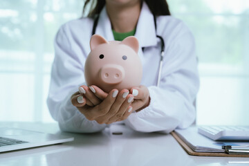 Close up young female general practitioner putting coin in piggy bank, managing hospital budget...