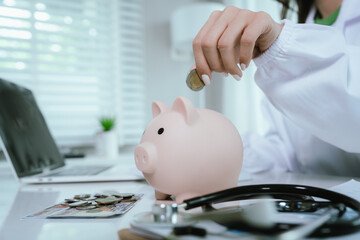 Close up young female general practitioner putting coin in piggy bank, managing hospital budget...