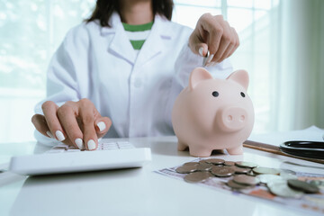 Close up young female general practitioner putting coin in piggy bank, managing hospital budget...
