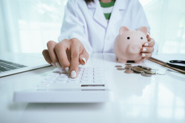 Close up young female general practitioner putting coin in piggy bank, managing hospital budget...