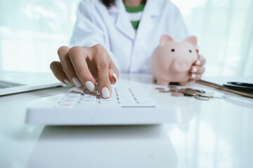 Close up young female general practitioner putting coin in piggy bank, managing hospital budget...