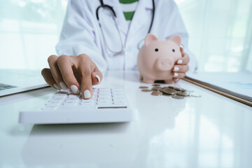 Close up young female general practitioner putting coin in piggy bank, managing hospital budget...