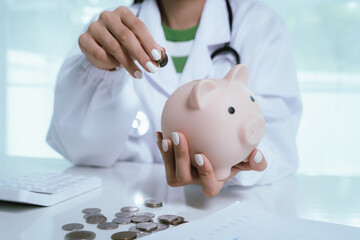 Close up young female general practitioner putting coin in piggy bank, managing hospital budget...