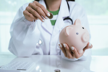 Close up young female general practitioner putting coin in piggy bank, managing hospital budget...