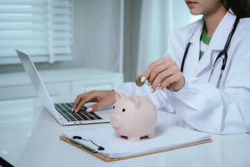 Close up young female general practitioner putting coin in piggy bank, managing hospital budget...