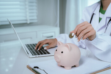 Close up young female general practitioner putting coin in piggy bank, managing hospital budget...