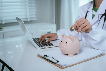 Close up young female general practitioner putting coin in piggy bank, managing hospital budget...
