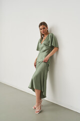 Stunning female model posing gracefully indoors in a stylish green dress