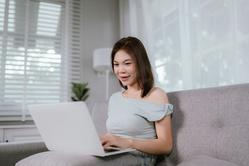 Fototapeta premium Asian woman makes online payments using credit card and laptop while sitting comfortably on sofa, managing finances or shopping from home.