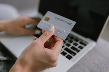 A woman makes an online payment using a credit card and laptop while sitting comfortably on a sofa, managing finances or shopping from home.