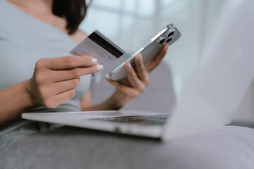 A woman makes an online payment using a credit card and laptop while sitting comfortably on a sofa, managing finances or shopping from home.